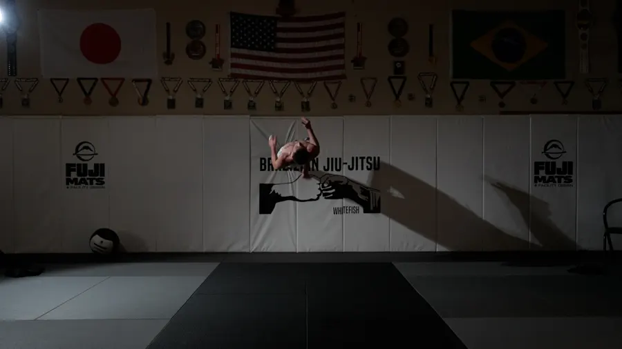 Coach Gage mid-flip in front of the Brazilian Jiu-Jitsu banner in the dimly lit gym