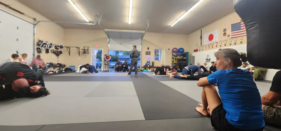 Wide view of a class in progress on the mats at Glacier Grappling & MMA, with members sitting along the wall