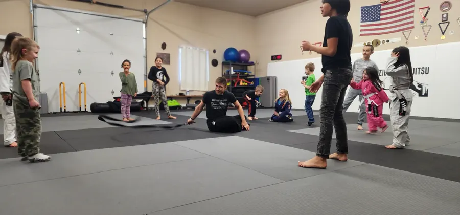 Kids class in full swing at Glacier Grappling & MMA, children in gis and a coach on the mats